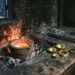A clay crucible of molten metal glowing in a bed of charcoal in a dark workshop, with three hammered gold bowls, a coil of gold bracelets and one dull iron bracelet waiting on the bench beside it.