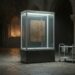 A sealed, softly lit glass and aluminium display case standing in a dark stone church interior, holding a plain blank wooden panel; a power cable runs from its base across the flagstones and an empty service trolley stands beside it.