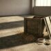 An empty unmarked wooden crate stands open on a bare concrete floor in raking light, loose straw spilled around it, a coil of rope and an open brass padlock beside it.