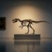 A dim auction-house gallery: a mounted small tyrannosaur skeleton on a low plinth under a single warm spotlight, with an old master painting in a gilt frame and a small bronze figure on a pedestal standing in shadow on the same bare wall.