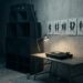 An empty dub dancehall after the night is over: a tower of black speaker cabinets, a single record on a turntable under a clip lamp, and a row of charcoal sketches of swaying dancers pinned to a bare wall.