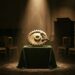 An empty auction saleroom at night, rows of gilt chairs in shadow and an unlit rostrum behind. On a green velvet-draped plinth under a single spotlight stands a large polished brass ratchet wheel with its pawl seated in the teeth, a mechanism that can only turn one way.