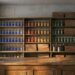 The interior of an old artists materials shop at closing time: a bare polished wooden counter, shelves of unlabelled glass jars of blue, red, yellow and green dry pigment, stacked plain wooden paint boxes, brushes in tin canisters, rolls of blank canvas, and bare plaster walls showing faint pale rectangles where pictures once hung.