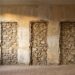 An empty Provencal salon with three tall rectangular voids cut out of the plaster wall, exposing bare stone and lath where painted panels were removed.